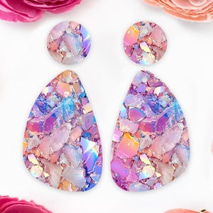 May include: A pair of iridescent pink and blue teardrop-shaped earrings with a shattered glass design. The earrings are made of resin and have a holographic finish.