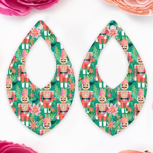May include: Two teardrop earrings with a festive nutcracker and floral design. The earrings have a green backdrop with red, pink, and yellow details. The nutcrackers are in red and gold uniforms.