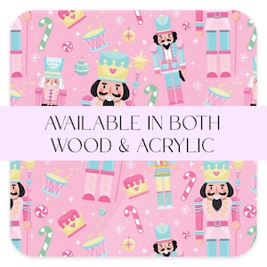 May include: A pink background with a repeating pattern of nutcrackers, candy canes, drums, and ornaments. The text "AVAILABLE IN BOTH WOOD & ACRYLIC" is displayed across the center of the image.