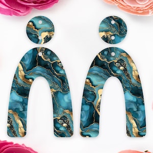 May include: A pair of blue and gold marble arch-shaped earrings. The earrings have a swirl pattern and are made of resin.