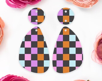 May include: A pair of checkerboard-patterned earrings. The earrings feature a black, orange, pink, light blue, and purple checkered design. The earrings are teardrop-shaped with a circular top. The earrings are displayed on a white background with pink flowers.