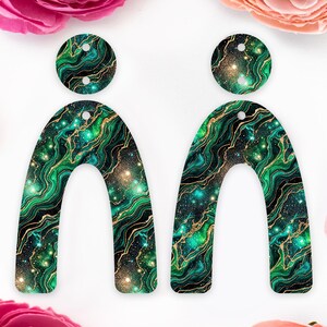 May include: A pair of earrings featuring a marbled pattern in green, black, and gold. Each earring has a circular top and a curved, arch shape. The design evokes a galaxy or gemstone appearance.