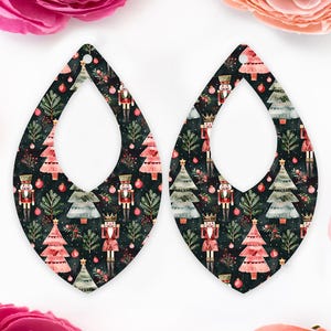 May include: Two teardrop earrings with a Christmas-themed design. The earrings display a dark background adorned with nutcrackers, Christmas trees, and baubles in red, green, and gold.