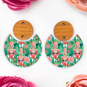 May include: A pair of earrings with a festive design. The earrings have a wooden top and a half-moon shape with a green background. The half-moon design is decorated with a repeating pattern of toy soldiers and floral elements.