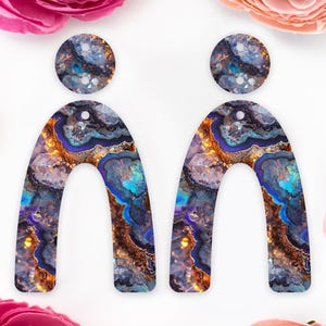May include: A pair of statement earrings with a unique agate design. The earrings are shaped like arches and feature a mix of blue, purple, gold, and white colours.