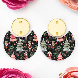 May include: A pair of festive earrings with a Christmas theme. Each earring has a gold-coloured top with two holes and a semi-circular bottom with a dark background. The bottom has a pattern of Christmas trees, nutcrackers, and baubles.