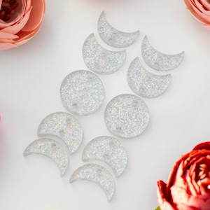 May include: A set of 10 silver glitter moon-shaped buttons. The buttons are various sizes and shapes, with some being full moons and others being crescent moons.