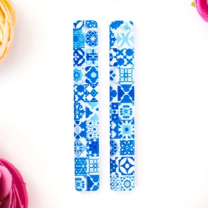 May include: Two blue and white patterned acrylic blanks for crafting. The blanks are rectangular and have a hole at the top.