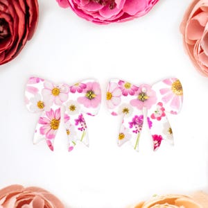 May include: A pair of white bow-shaped earrings with a pink floral print.
