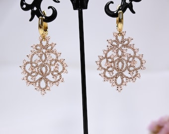 May include: A pair of gold-tone dangle earrings with a delicate, intricate design featuring a filigree pattern and clear crystals.