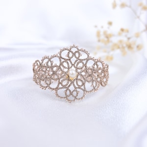 May include: A delicate, intricate lace bracelet with a pearl accent. The bracelet is made of a fine, woven material and has a delicate, feminine design.