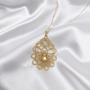 May include: A gold chain necklace with a delicate, intricate pendant featuring a gold filigree design and a clear, faceted gemstone in the center.