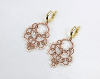 May include: A pair of gold-coloured drop earrings with an intricate, openwork design. The earrings feature a copper-coloured filigree pattern with small, white beads. The earrings have gold-coloured lever-back closures.