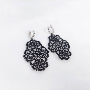 May include: A pair of black lace earrings with silver hooks. The earrings are delicate and intricate, with a floral design.