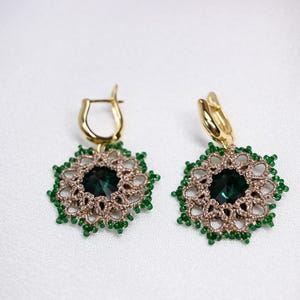 May include: A pair of gold earrings with green and brown beaded details and a green gemstone in the centre of each earring.