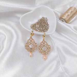 May include: A pair of gold earrings with a delicate, intricate design. Each earring features a small, round pearl pendant.