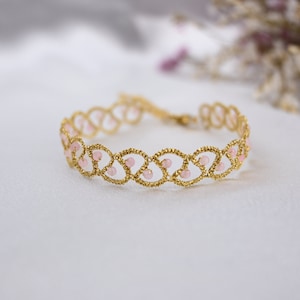Pode incluir: Uma pulseira dourada com um design delicado e intrincado com contas cor-de-rosa. A pulseira é feita de um material fino e flexível e tem um visual delicado e feminino.