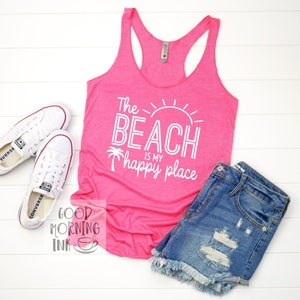May include: A bright pink tank top with the text "The BEACH is my happy place" in white, paired with denim shorts and white sneakers. The top has a racerback design, perfect for a day at the beach.