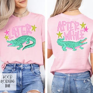 以下が含まれることがあります： 前面にターコイズのアリゲーターのグラフィックとピンク色の「LATER」という文字が入ったピンク色のTシャツ。Tシャツの背面には「AFTER WHILE」という文字と、お揃いのアリゲーターのグラフィックが入っています。シャツには緑とピンクの星のアクセントも付いています。