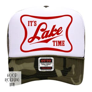 May include: A white and camouflage trucker hat with the text "IT'S Lake TIME" in red. The hat features a white front panel with a red curved border around the text. The brim is camouflage, and the hat has a mesh back.