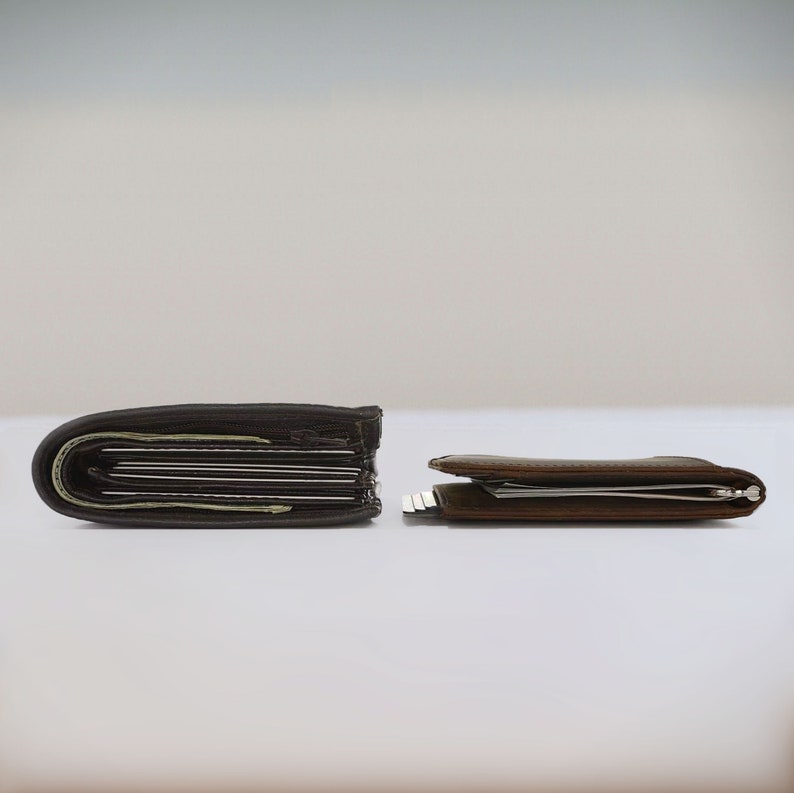 Two dark brown slim leather bifold wallets lay on top of a desk side by side. The view is from the side to show a comparison in size between the two leather bifold wallets for men. The wallet on the left is about double the height of the slim wallet on the right.