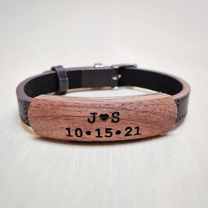 May include: A brown leather bracelet with a wooden inlay. The inlay is engraved with the initials "J♥S" and the date "10.15.21".