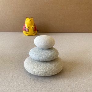 May include: A stack of three smooth, gray stones, balanced on top of each other. The stones are arranged in a pyramid shape, with the largest stone at the bottom and the smallest stone at the top.