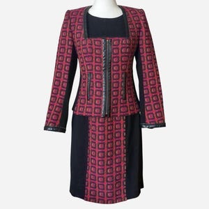 May include: A two-piece suit featuring a jacket and skirt. The jacket has a square neckline, a zipper, and a geometric pattern in red and black. The skirt is black with a matching geometric pattern.