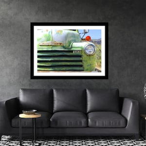 May include: Close-up of a framed print featuring a vintage green truck. The truck's front grill and headlight are visible, with a weathered, aged appearance. The image is displayed on a dark gray wall above a black leather sofa.