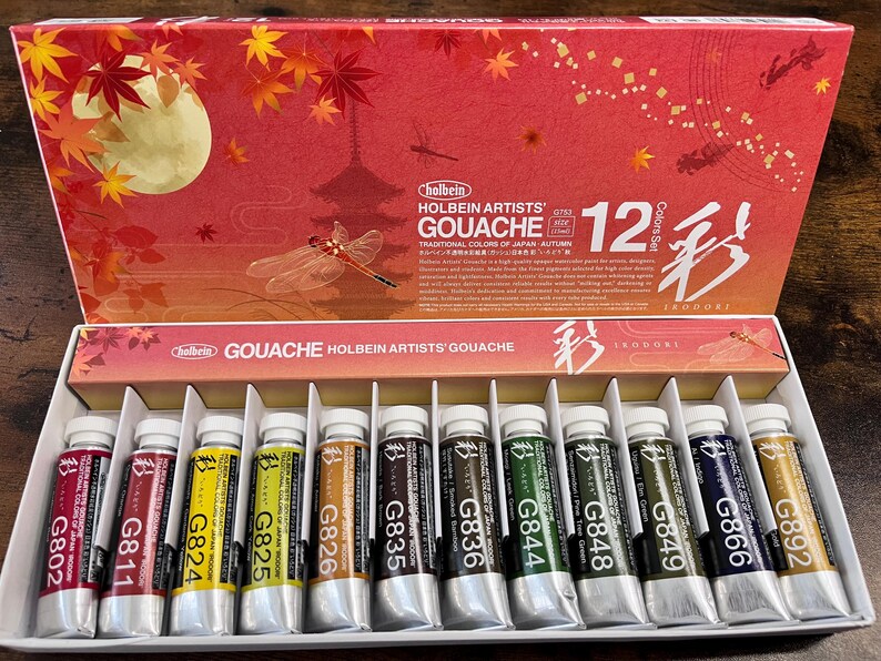 May include: A set of 12 Holbein Artists' Gouache paints in tubes. The tubes are arranged in a row and labeled with numbers and colors. The paint set is packaged in a box with a Japanese-inspired design featuring a dragonfly and the text "12 Colors Set" and "IrodorI".