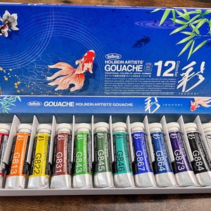May include: A set of 12 Holbein Artists' Gouache paints in tubes. The tubes are labeled with the color number and name. The set is packaged in a blue box with a Japanese-inspired design. The box features a gold fish and the text "Holbein Artists' Gouache 12 Color Set Irodori."