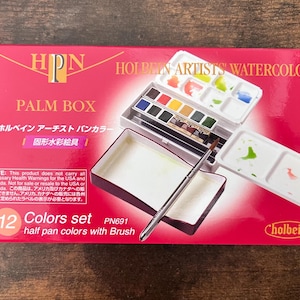 May include: A red Holbein Artists' Watercolor Palm Box set. The box contains 12 half-pan watercolor paints, a brush, and mixing palettes. The box is labeled with Japanese text and the text "12 Colors set".