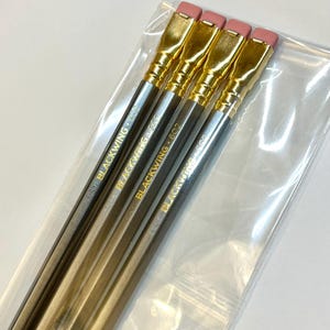 May include: Four gold and silver pencils with pink erasers and gold accents. The pencils are labeled "Blackwing 602".