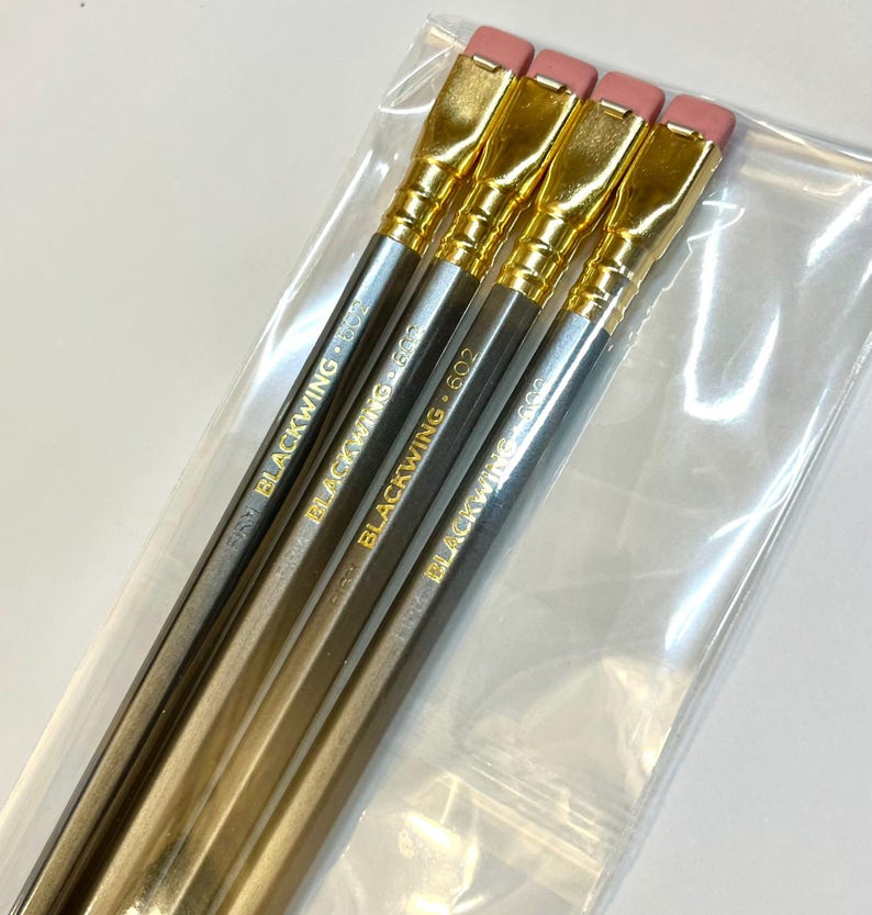 May include: Four gold and silver pencils with pink erasers and gold accents. The pencils are labeled "Blackwing 602".