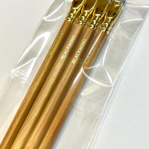May include: Four wooden pencils with gold-colored tops and gray erasers. The pencils are packaged in a clear plastic bag. The pencils are labeled "Blackwing" in gold lettering.