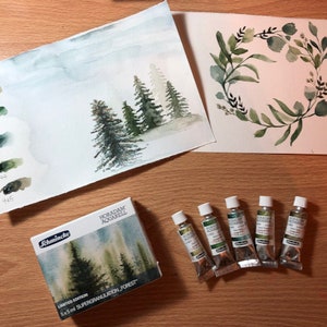 May include: A set of five 5 ml tubes of green watercolor paint, labeled "HORADAM Aquarell" and "Schmincke", with a box of watercolor paints labeled "Limited Edition 5x5ml Supergranulation - Forest". The box shows a watercolor painting of a forest scene. There are two watercolor paintings on paper, one of a forest scene and one of a green wreath.