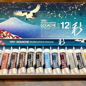May include: A set of 12 Holbein Artists' Gouache paints in tubes. The tubes are labeled with the color number and name. The set is packaged in a box with a Japanese-inspired design featuring a crane and a mountain.