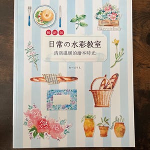 May include: A book cover with a light blue and white striped background, featuring watercolor illustrations of food, flowers, and utensils. The title is in Japanese, with the text "Watercolor Classroom" and "Abe Marie".
