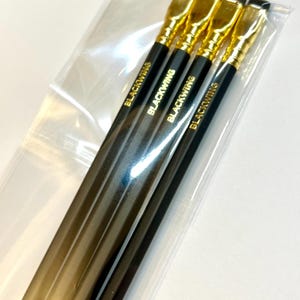 May include: Four black pencils with gold accents and the word "Blackwing" printed on each pencil. The pencils are packaged in a clear plastic bag.