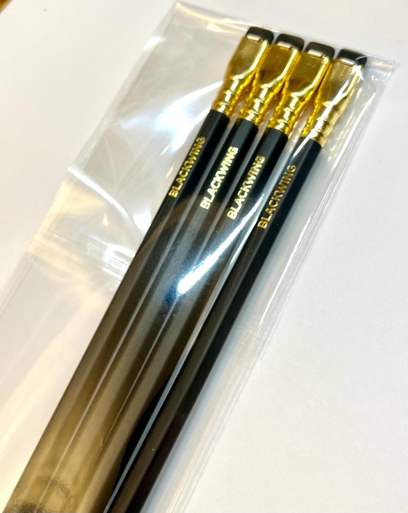 May include: Four black pencils with gold accents and the word "Blackwing" printed on each pencil. The pencils are packaged in a clear plastic bag.