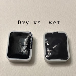 May include: Two small square pans of black watercolor paint, one dry and one wet. The text "Dry vs. wet" is written above the pans.