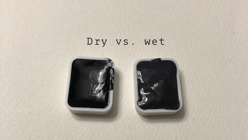 May include: Two small square pans of black watercolor paint, one dry and one wet. The text "Dry vs. wet" is written above the pans.