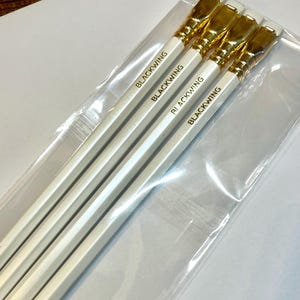 May include: Four white pencils with gold-colored erasers and the word "BLACKWING" printed in gold on each pencil.