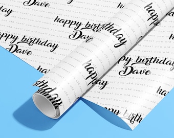 May include: White wrapping paper with a repeating pattern of the text "happy birthday Dave" in black cursive writing. The paper is rolled up and partially unrolled, revealing the pattern.