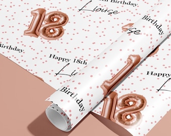 May include: White wrapping paper with a pattern of small pink dots and rose gold number 18 balloons. The words "Happy 18th Birthday" and the name "Louise" are printed in black script. A roll of the paper is visible.