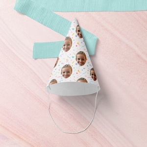 May include: A white party hat with a colorful confetti pattern and a repeated image of a child's face. The hat has a white string attached to the top.