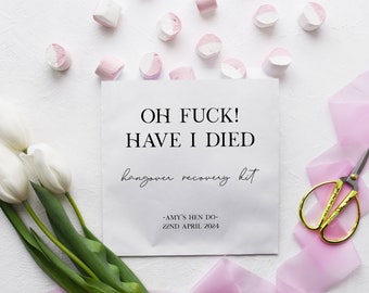 May include: White paper bag with the text "OH FUCK! HAVE I DIED hangover recovery kit -AMY'S HEN DO- 22ND APRIL 2024" printed on it. The bag is surrounded by white and pink marshmallows, white tulips, pink ribbon, and gold scissors.