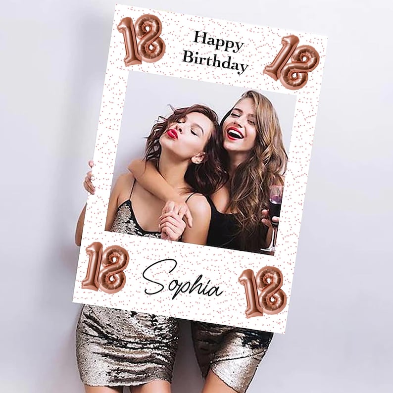Op de afbeelding: Een witte fotolijst met de tekst "Happy Birthday" en "Sophia" in zwart schrift. Het nummer "18" wordt herhaald in ros&eacute;gouden ballonlettertype. Twee vrouwen staan in de lijst, glimlachen en omarmen elkaar. De lijst heeft een stippenpatroon.