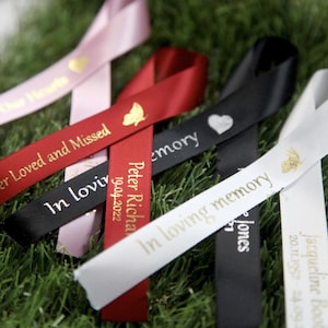May include: Assortment of black, white and red satin ribbons with gold lettering. The ribbons have different messages, including "In loving memory", "Peter Richard", and "er Loved and Missed".