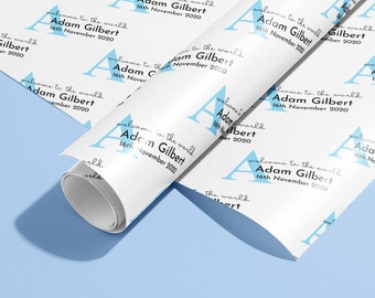 May include: White wrapping paper with a repeating pattern of blue stylized letter A's and the text "Welcome to the world Adam Gilbert 16th November 2020".